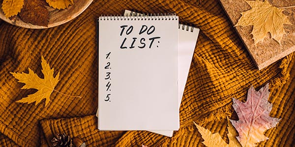 Spiral notebook with "TO DO LIST:" and numbers 1 through 5 resting on a mustard yellow blanket surrounded by autumn leaves.
